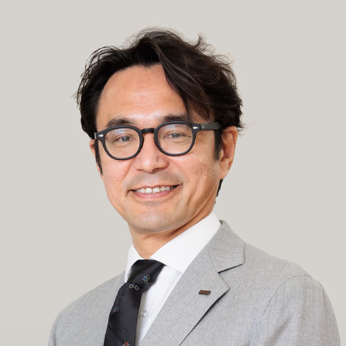 KDDI Digital Divergence Holdings代表取締役社長 CEO、藤井 彰人の写真。グレーのスーツを着て黒淵の眼鏡をかけています。